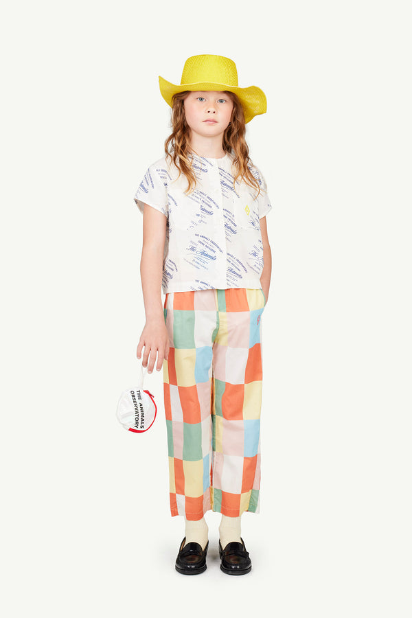 In the image, a kid is wearing camel pants with white squares and a short-sleeve white baboon shirt. These products are part of The Animals Observatory Spring-Summer 2024 collection.